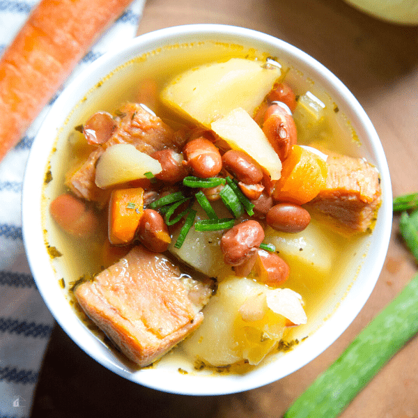 Potato and ham soup served in a white bowl, topped with green onions.