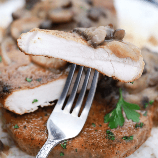 Fork with piece of pork chop with mushroom gravy.