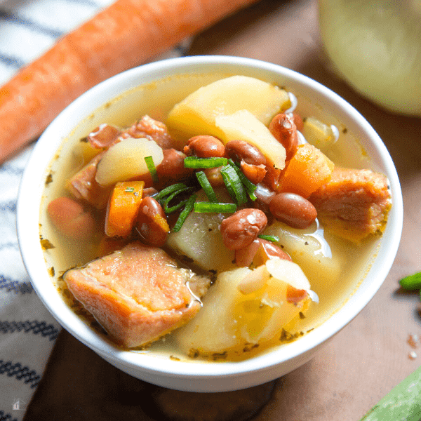 Ham, bean and potato soup served in a white bowl.