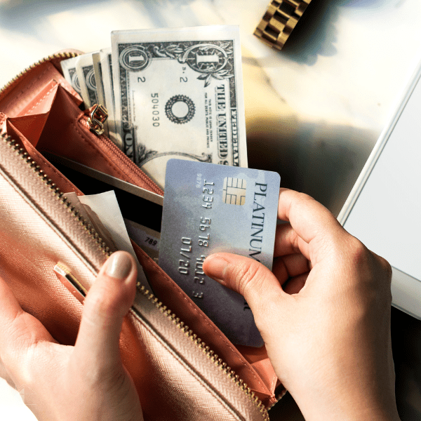 Woman pulling a credit card and cash from her brown wallet.