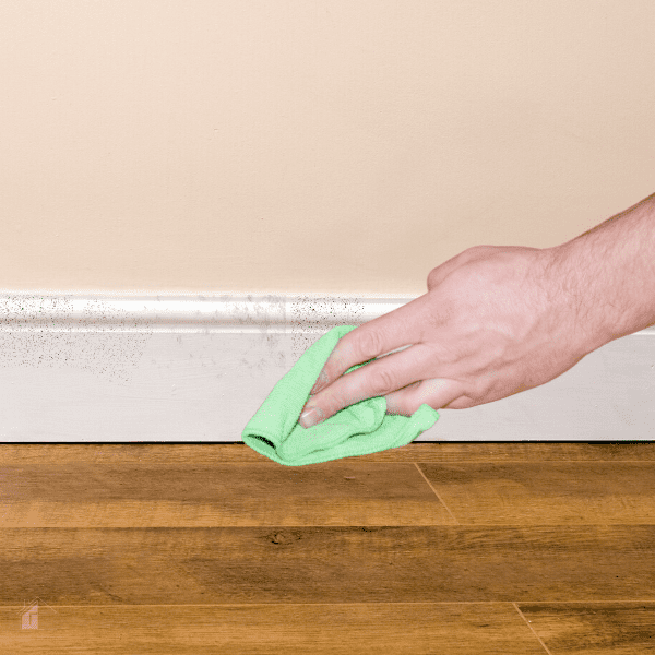 Male hand using a green microfiber cloth to clean dirty white baseboards.