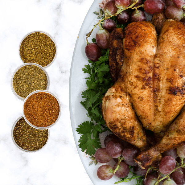 Four bowls full of seasons and a cooked season trukey next to them plated with grapes and cilantro as base.