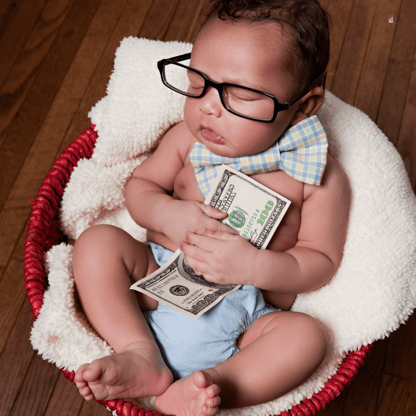 Newborn baby sleeping in a basket holding a one hundred dollar bill.