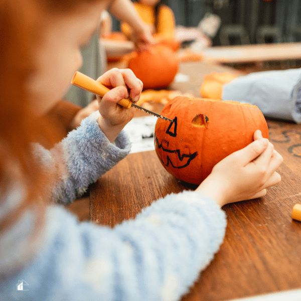 Little girl carving a pumpking on a table.