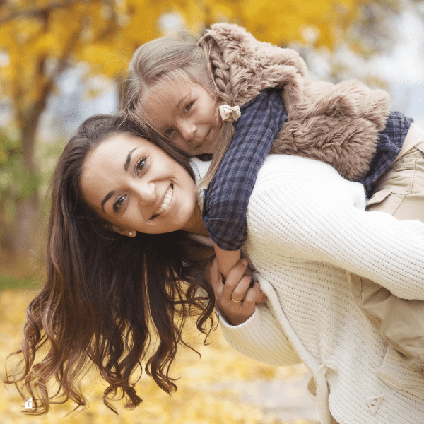 Young mom with daugher on her back outdoors in the fall season.