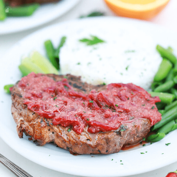 Close up of served pork steak topped with red sauce. mashed potatos on the side and green beans.
