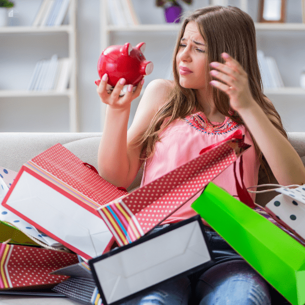 Young Woman with Shopping Bags sitting in her living room and holding red piggy bank.