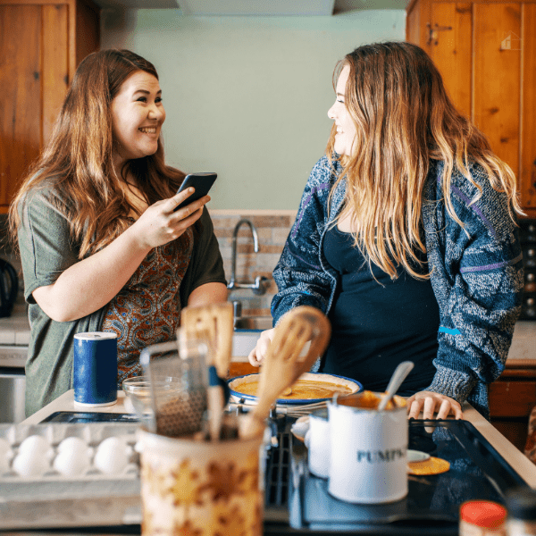 Two young woman using their smartphone to follow an online recipe and make pumpkin pie.