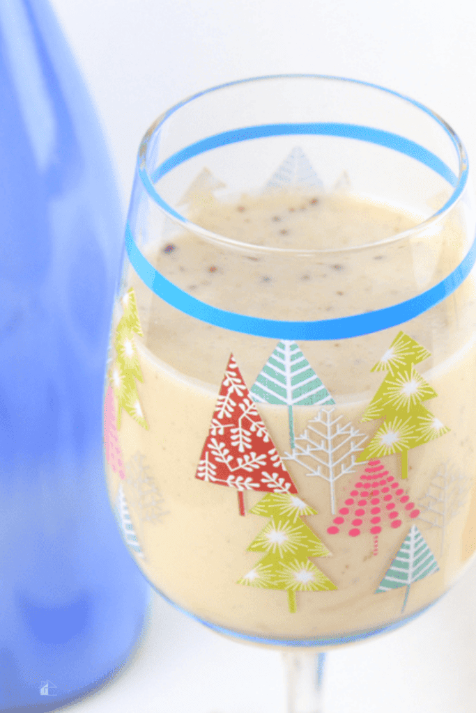 Glass of Puerto Rican Coquito without eggs, garnished with a cinnamon stick and surrounded by festive holiday decor, highlighting the creamy texture and rich coconut-based drink perfect for Christmas celebrations.