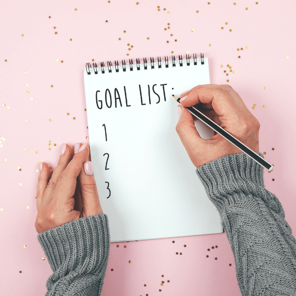 woman writing goals on notebook.