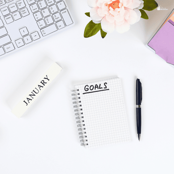 Write a Goal for the New Year in a White Notebook on a White Desktop Next to a Coffee Mug and a Keyboard