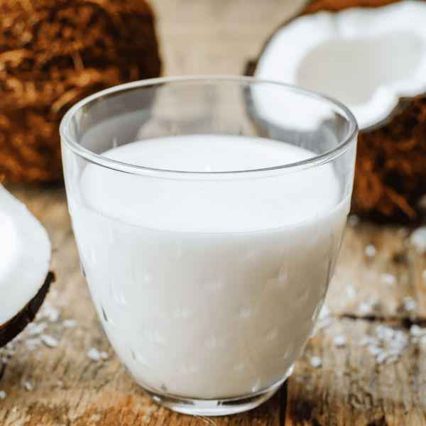 Coconut milk in a glass and coconuts on a dark wood background.