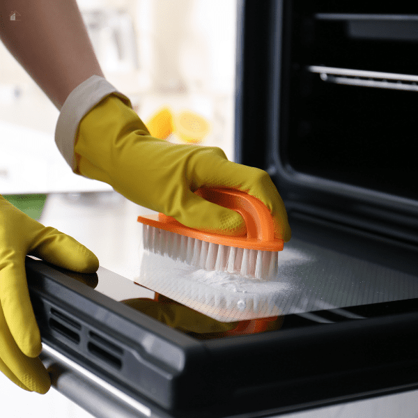 Woman cleaning overn door with baking soda.