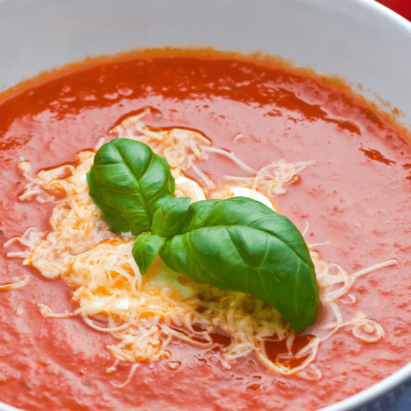 Homemade tomato soup served on white bowl and garnished with basil.