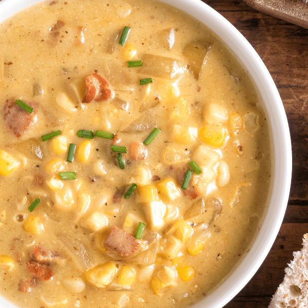 Homemade corn soup with bacon served with bread on a rustic wood table.