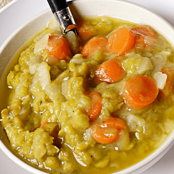 Split pea soup in white bowl with spoon, ready to eat.