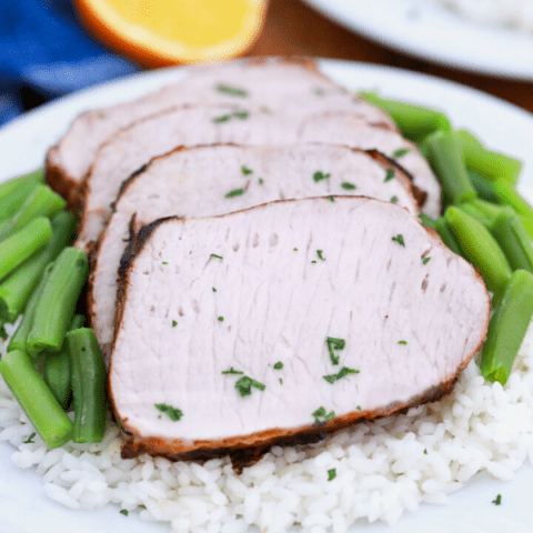 four slices of pork loin served over white rice adn green beans.