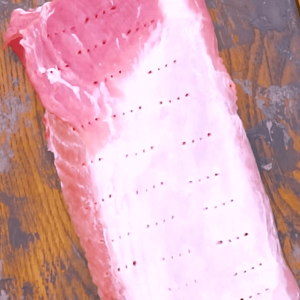 Raw pork loin with fork holes ready to be marinated.