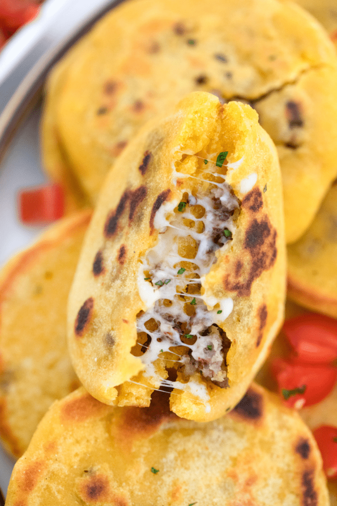 An opened pupusa exposing ground beef and cheese inside.