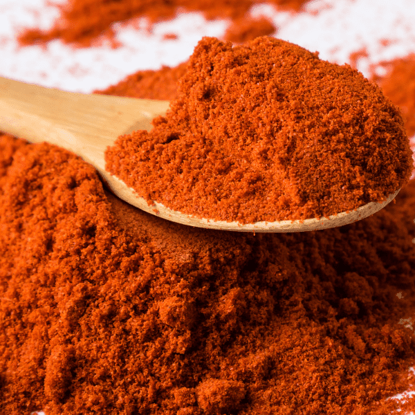 Red paprika spice powder on white table with spoon.