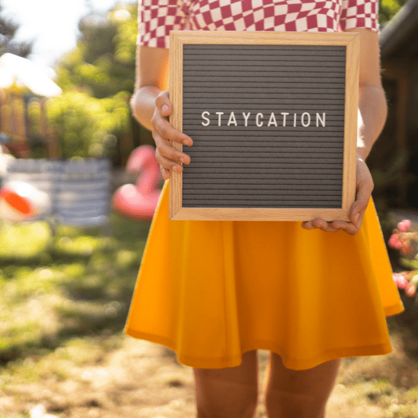 woman holding a sign that says Staycation in the back yard.