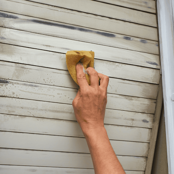 Hand holding a sponge and cleaning a dirty blind of a window.