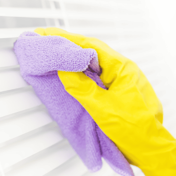 Hand holding a sponge and cleaning a dirty blind of a window.