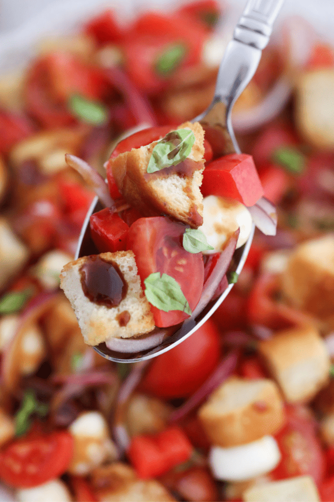 Close up spoon full of Panzanella with a panzanella salad in the background.