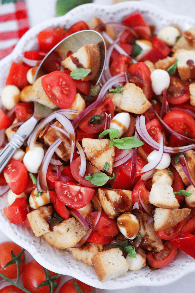 A closeup panzanella salad in a white bowl with a spoon.