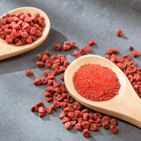 Annatto powder in a sppon with seeds next to it.