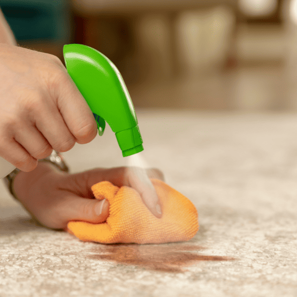 removing stain from carpet with sprayer and orange cloth.