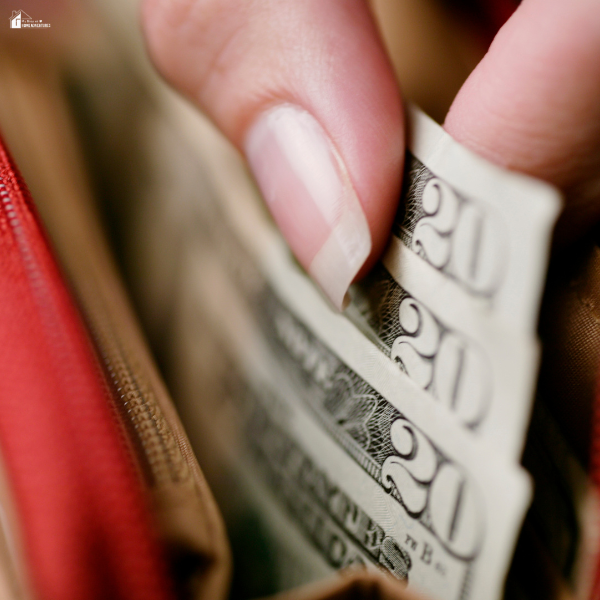 Hand pulling cash from a wallet showing simple ways to save money during the summer season.