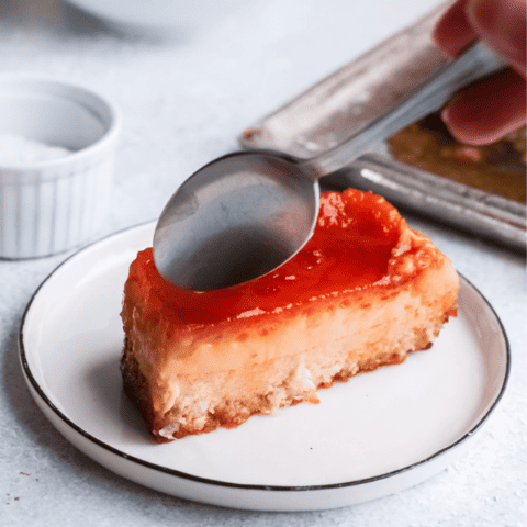 Close-up of a piece of coconut flan on a plate with a spoon hovering above it.