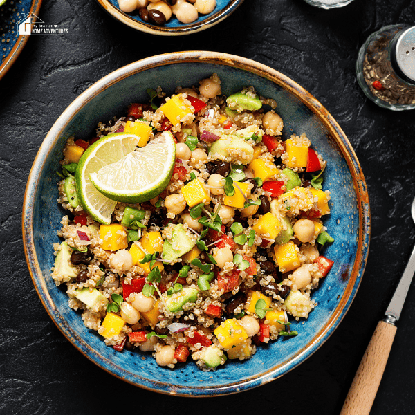 An image of a quinoa and black bean salad. Included in the image is a pepper shaker, a fork, and a part of a bean bowl.