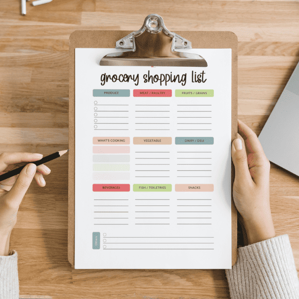 Female hand holding a clipboard with a blank shopping list printable.