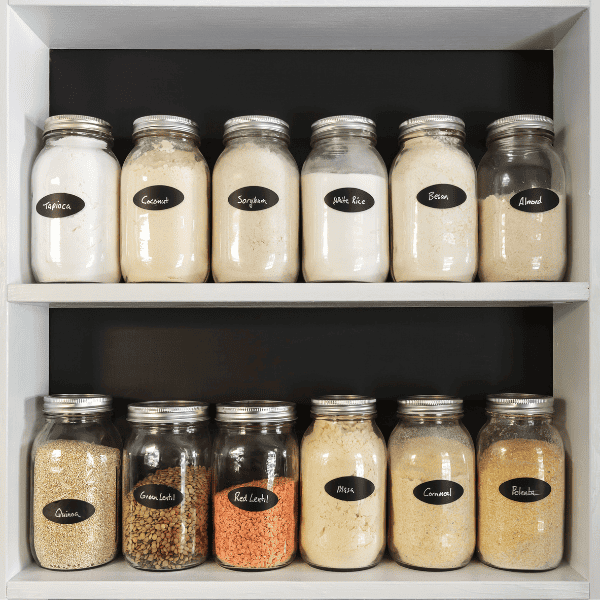 Jars of flours and grains on white shelves in pantry.