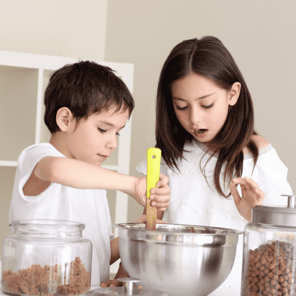 Boy and girl in the kitchen stiring something in a large bowl.