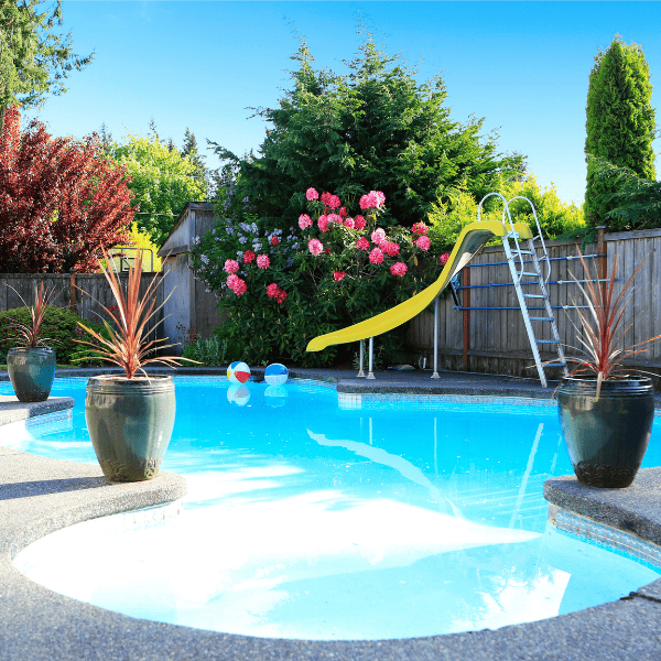 Fenced backyard with small beautiful swimming pool and slide.