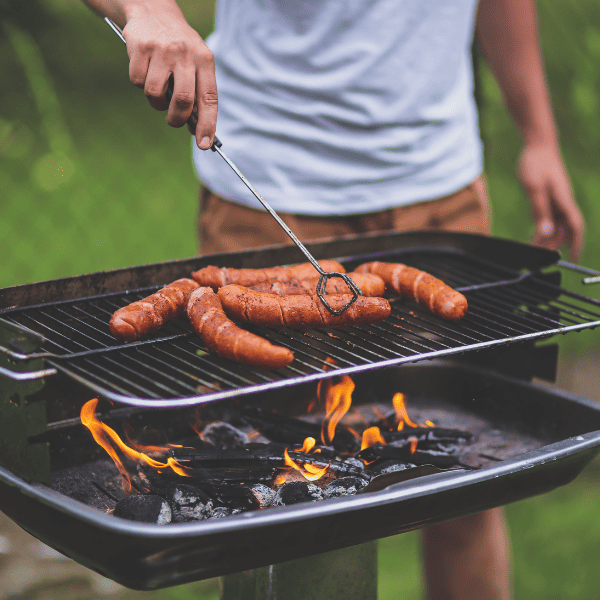 A man grilling hot dogs using a charcoal grill.