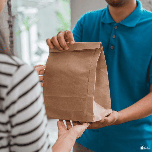 A customer receiving a takeout food order in a paper bag, representing an expense that may be reduced when money is tight.
