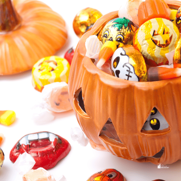 an orange pumpkin filled with Halloween pumpkin candies with text: "How Much Should You Spend On Halloween Candy"