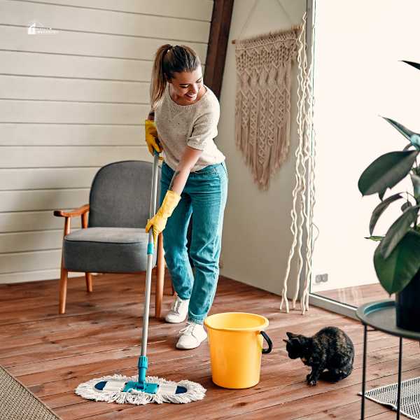 a woman mopping the floor with a cat near her
