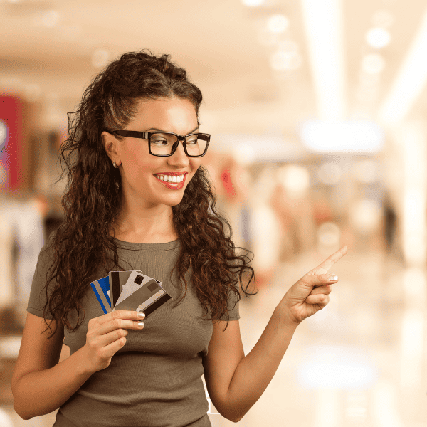 Woman holding credit cards in one hand and pointing at something at the mall.