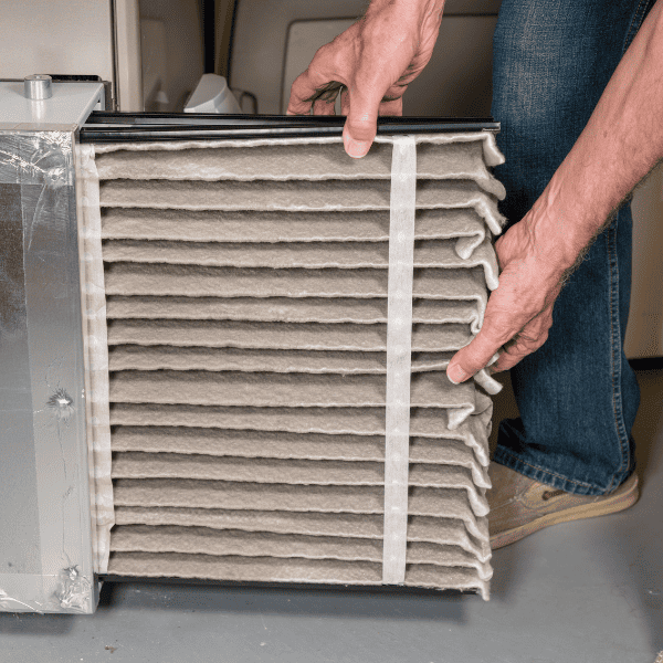 Man changing a folded dirty air filter in the HVAC furnace ystem in the basement.