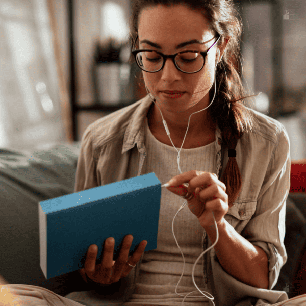 woman holding a book and earphones while relaxing in her living room.