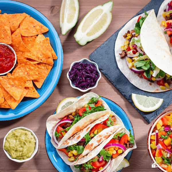 An image of tacos, nachos, guacamole, salsa, and lime slices.