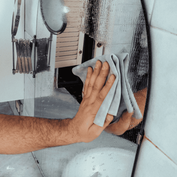 Cheerful man cleaning bathroom mirror