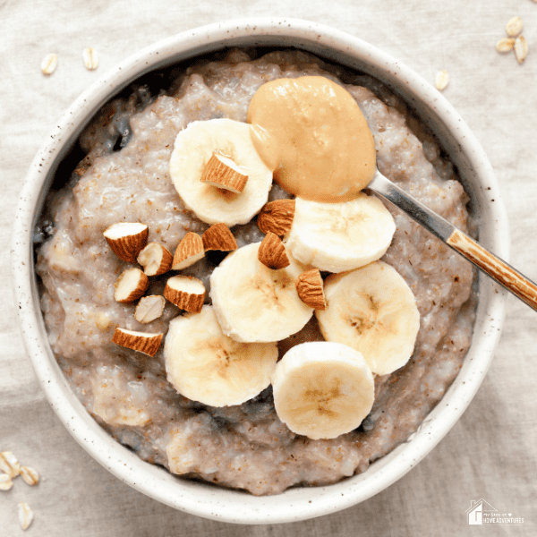 An image of a bowl of oatmeal, with banana slices, almond bits, and a spoonful of peanut butter.