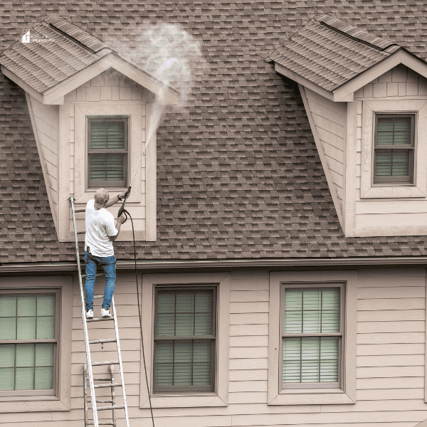 Worker on Ladder Pressure Washing Home