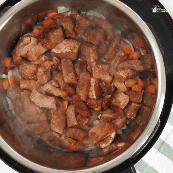 An image of meat, carrots, and onions in a pressure cooker.